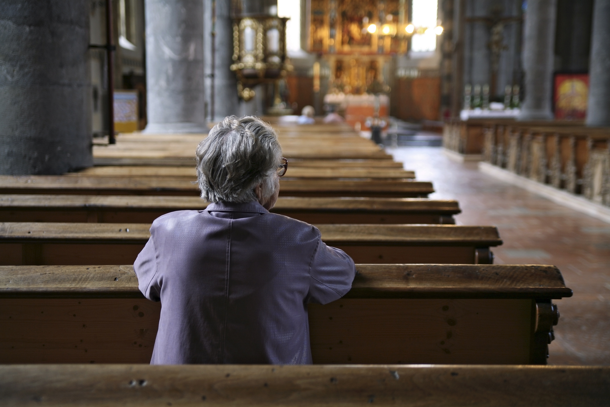 Older woman praying in an almost empty church, rear view